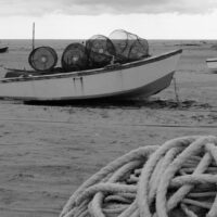 Barca a terra in spiaggia con corde intrecciate in primo piano e involucri cilindrici sullo sfondo, paesaggio marino.