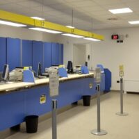 Interno di ufficio postale: banconiazzurri, sportelli, orologio digitale, segnaletica e clienti in attesa nell’area servita.