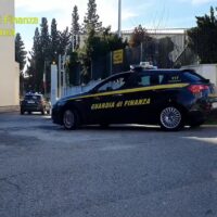 Auto della polizia in divisa blu, con scritta G.O.D.O.P. su fiancata, parcheggiata su strada di quartiere con edifici e alberi sullo sfondo.