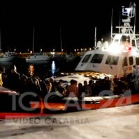 Imbarcazione della guardia costiera al molo notturno con fusili e soccorritori pronti all’intervento