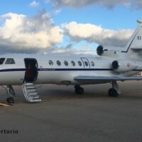 Aereo di business jet bianco con porte aperte e scaletta, pronto al decollo su una pista soleggiata, nuvole in cielo.
