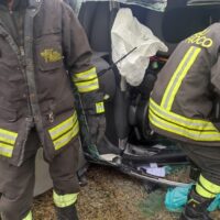 Due vigili del fuoco in divisa giallo-neri all’esterno di un veicolo danneggiato, attrezzature e sedili visibili nel vano