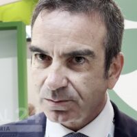 Primo piano di un uomo serio in giacca, con sfondo verde e lucentezza professionale.